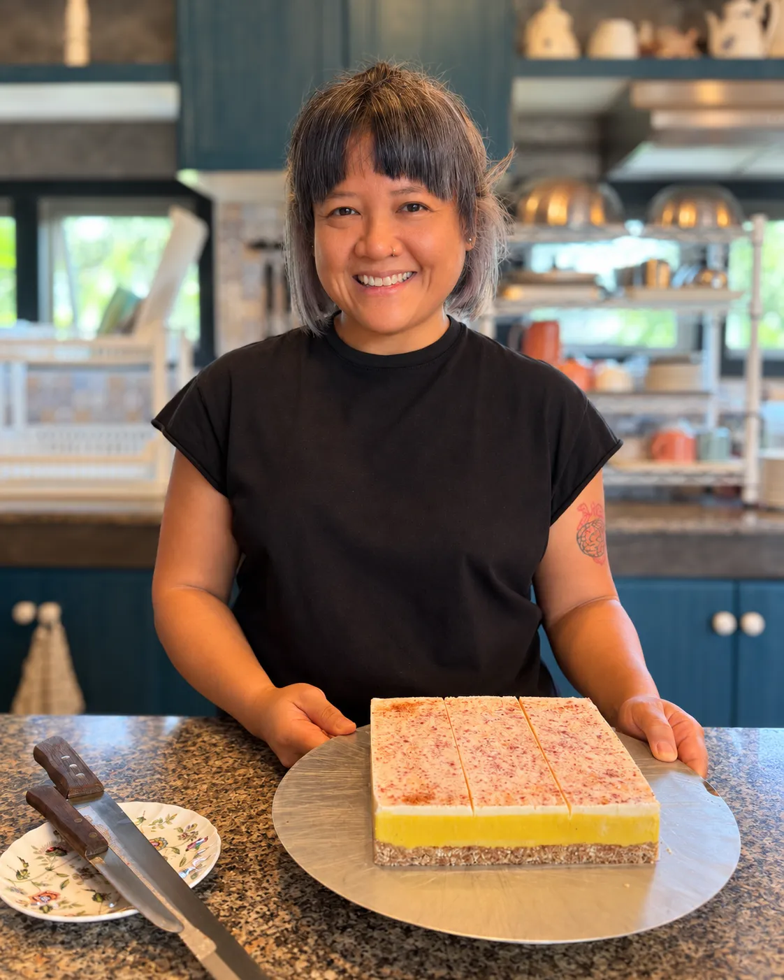 Ploy smiling in her kitchen, holding a raw layered cake