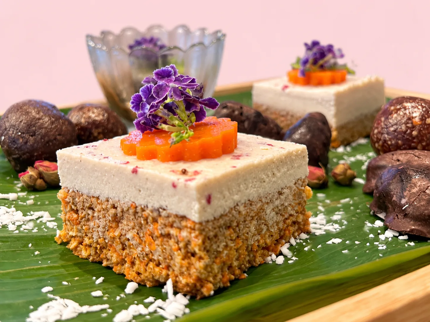 A slice of raw carrot cake with cashew frosting, topped with a carrot flower and purple flowers