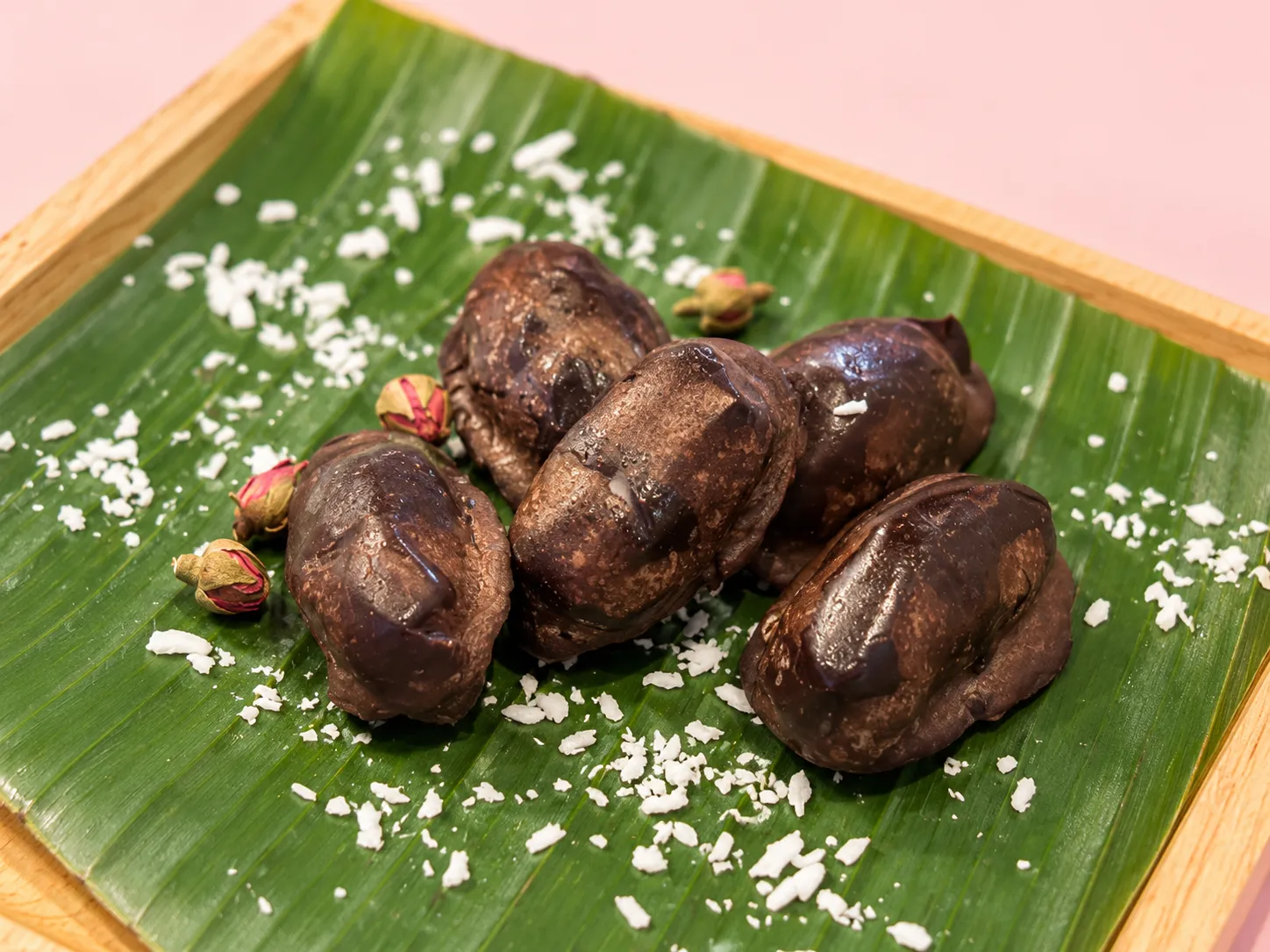Chocolate-covered dates on a banana leaf with coconut flakes and dried rosebuds