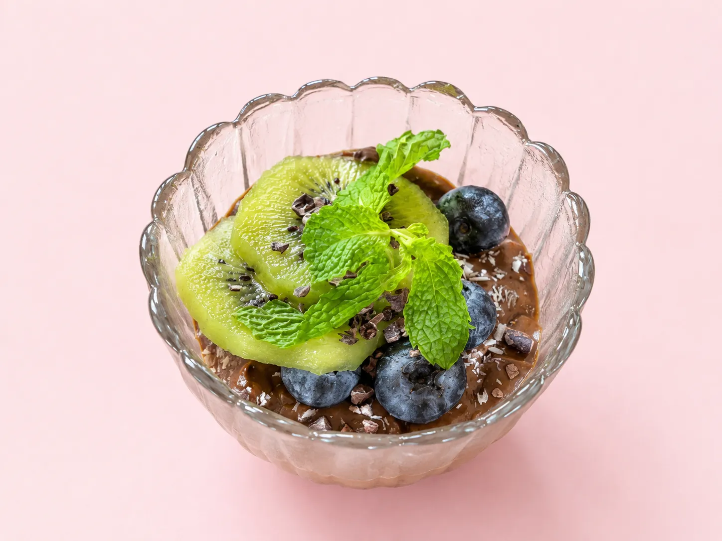 Chocolate avocado mousse in a glass bowl, topped with kiwi, blueberries, mint and cacao nibs
